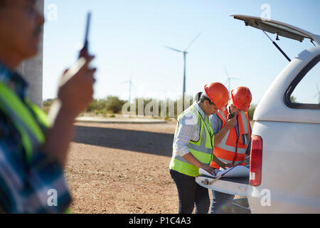 Engineers reviewing blueprints at truck at sunny wind turbine power plant Stock Photo
