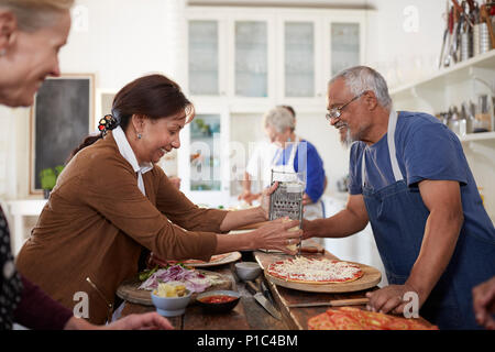 Senior couple shredding cheese over fresh pizza in cooking class Stock Photo