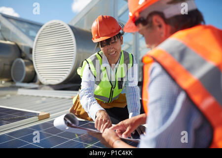 Engineers with clipboard examining solar panel at sunny power plant Stock Photo