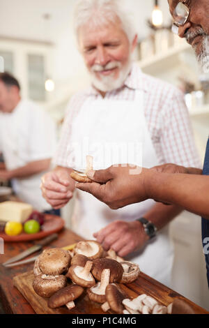 Senior men friends slicing fresh mushrooms in cooking class Stock Photo