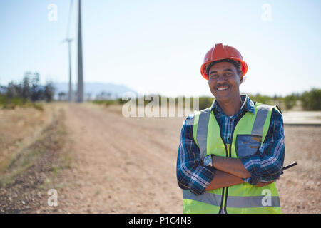 Portrait smiling engineer on dirt road at wind turbine power plant Stock Photo