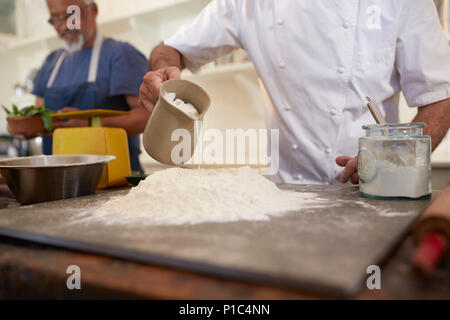 Close up chef pouring water into pizza dough flour nest in cooking class Stock Photo