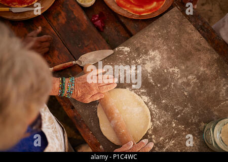 Overhead view senior woman rolling, making fresh pizza dough Stock Photo