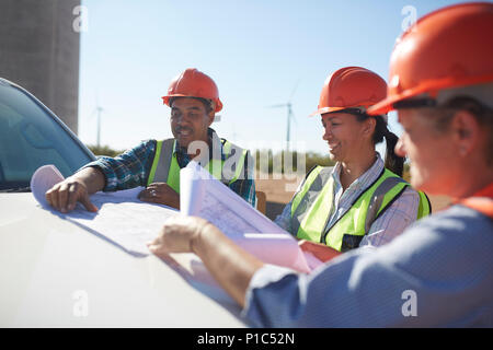 Engineers reviewing blueprints on truck at sunny wind turbine power plant Stock Photo