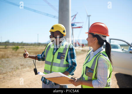 Engineers with blueprints talking at sunny power plant Stock Photo