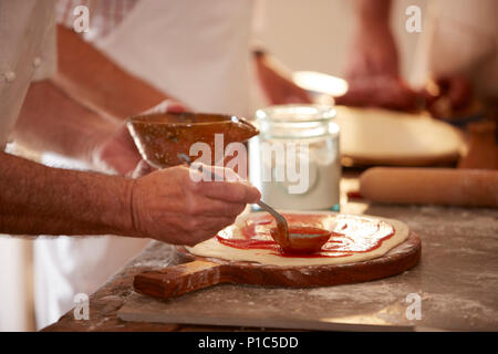 Close up man spreading marinara sauce on dough in pizza cooking class Stock Photo