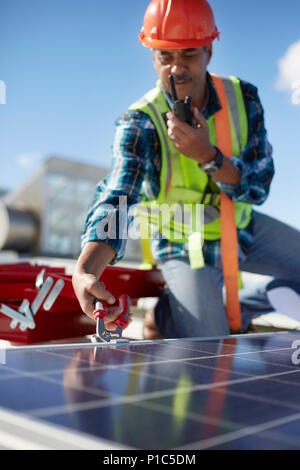 Male engineer with walkie-talkie repairing solar panel at power plant Stock Photo