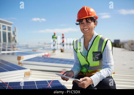 Portrait smiling, confident female engineer with digital tablet inspecting solar panels at sunny power plant Stock Photo