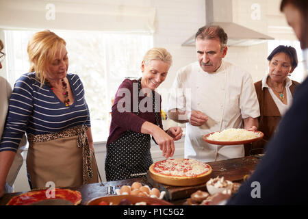 Chef and senior friends making pizza, spreading cheese in cooking class Stock Photo