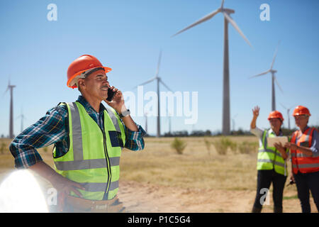 Smiling engineer talking on cell phone at sunny wind turbine power plant Stock Photo