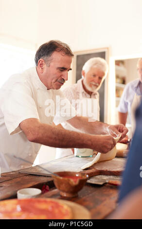 Focused chef spreading pizza dough in cooking class Stock Photo