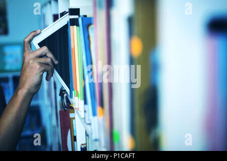 Hand of student keeping digital tablet in bookshelf in library Stock Photo