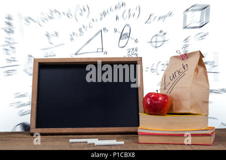 Slate with chalks by lunch bag and books on wooden table Stock Photo