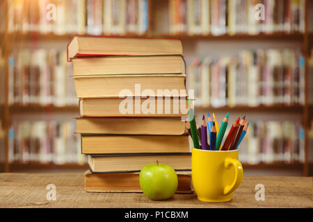 Composite image of stack of books by colored pencils in mug and apple on table Stock Photo