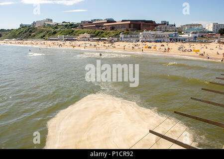 Brown sea algae blooming more than usual in early summer off the south coast. The smelly, unsightly and frothy algal bloom, seen here pooling on the sea beneath the pier, is considered harmless to swimmers and bathers. Bournemouth, Dorset, England, UK, 11th June 2018. Stock Photo