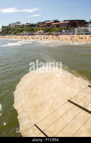 Brown sea algae blooming more than usual in early summer off the south coast. The smelly, unsightly and frothy algal bloom, seen here pooling on the sea beneath the pier, is considered harmless to swimmers and bathers. Bournemouth, Dorset, England, UK, 11th June 2018. Stock Photo