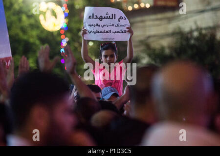A young girl holds a sign as a crowd marches down the street during a protest against Mahmoud Abass. Palestinians gathered in Al-Manara Square to march in protest of Mahmoud Abass and the Palestinian Authority. A group of pro-Abass supporters briefly scuffled with protesters, however the march remained peaceful after. Stock Photo