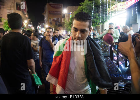 A protester wearing the Palestinian flag as a cape joins in the protests against Mahmoud Abass. Palestinians gathered in Al-Manara Square to march in protest of Mahmoud Abass and the Palestinian Authority. A group of pro-Abass supporters briefly scuffled with protesters, however the march remained peaceful after. Stock Photo