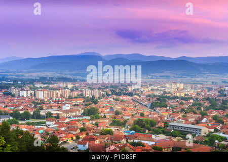 Colorful purple sunset sky over Pirot city in Serbia and golden, sunlit buildings Stock Photo
