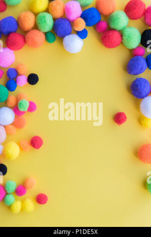 Bright multi-colored pom-poms arranged as a border on a solid yellow background Stock Photo