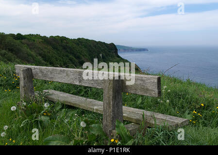 Old weathered wooden bench looking out to sea with beautiful blue sky from Ravenscar, North Yorkshire. Stock Photo