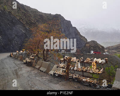 Road in the High Atlas Mountains: among the rocks passes a strip of asphalt, lonely trees, Morocco. Stock Photo