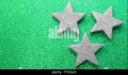 three large silver stars on green glittery background Stock Photo