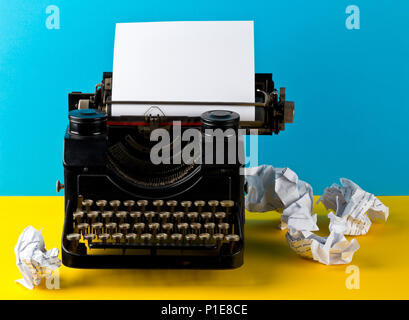 Vintage typewriter with empty, blank sheet of paper and crumbled paper balls on yellow and cyan background Stock Photo