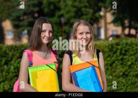 Two girls schoolgirl. Summer in nature. Smile happily. Ready for school lessons. In hands of a folder with notebooks. He rests after school. Best girlfriends. Stock Photo