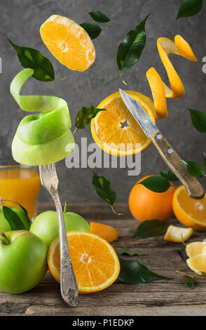 Levitating fresh sliced fruit, apple and orange with fork and knife isolated on wooden background. Stock Photo