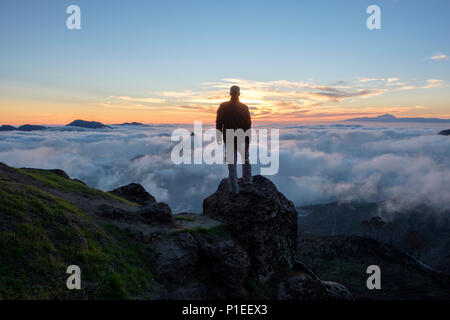 Man looks at Roque Bentayga and Teide above the clouds at sunset, Gran Canaria, Canary Islands, Spain Stock Photo