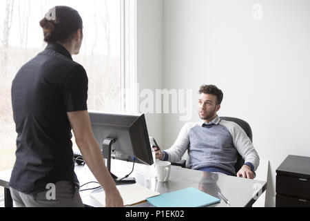 Two young businessmen confer at a desk in a modern office. Stock Photo