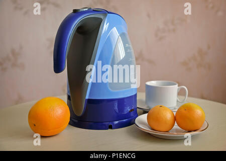 On the table is an electric kettle, next are oranges and tangerines. Stock Photo