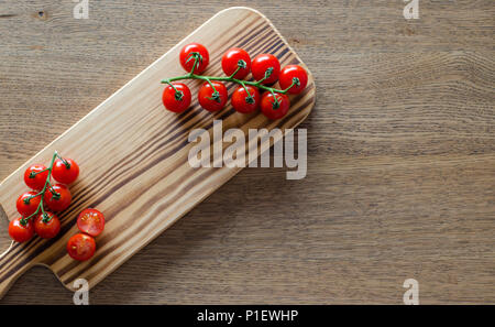 A branch of cherry tomatoes on wooden cutting board. selective focus. top view. pattern with place for text Stock Photo
