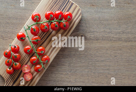 A branch of cherry tomatoes on wooden cutting board. selective focus. top view. pattern with place for text Stock Photo