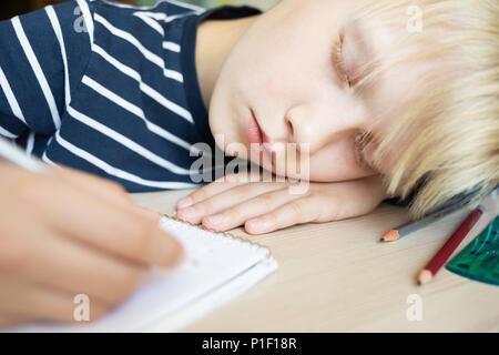 Boy sleeping on the desk while doing his homework in notebook. Close up. Stock Photo