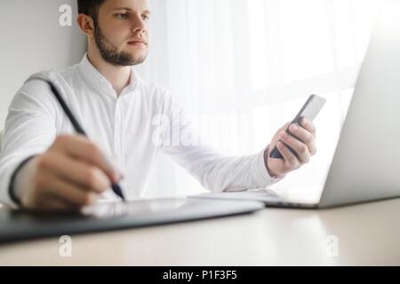 Young smiling bearded businessman is working on computer holding Stock Photo