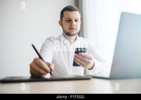 Young Man sitting at a table at home working on a laptop compute Stock Photo