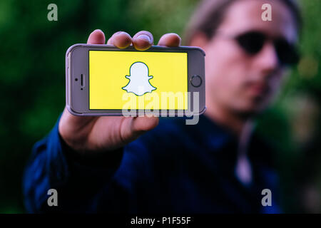 Closeup of serious young man with sunglasses holding white iPhone with SNAPCHAT LOGO on screen Stock Photo