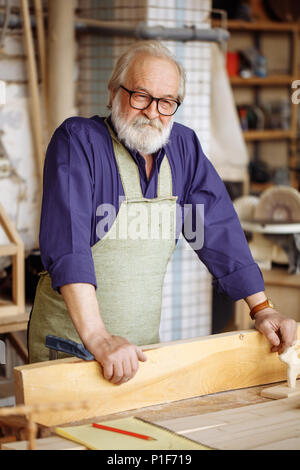 old man in glasses and casual clothes likes to work with wood Stock Photo