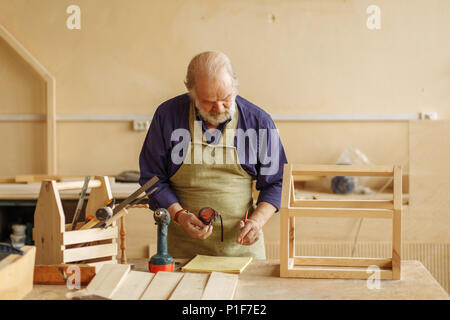 old craftsperson holding tape measure and writing something in the exercise book Stock Photo