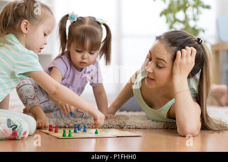 Happy family. Young mother playing ludo boardgame with her daughters while spending time together at home. Stock Photo