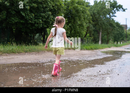 Little girl walking along the wet broken road after the rain. Stories about rural life in Ukraine Stock Photo