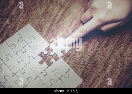 Close up of hand placing the last jigsaw puzzle piece, Hand holding missing jigsaw puzzle piece down in to the place, conceptual of problem solving, f Stock Photo
