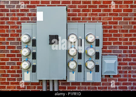 Straight on horizontal shot of electric meters attached to the outside red brick wall of a multi-family apartment building. Stock Photo