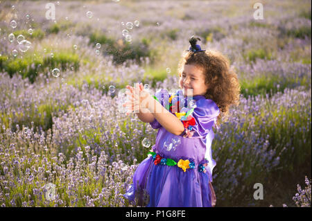 pretty little girl in fairy hat and dress playing with soap bubbles in lavender field Stock Photo