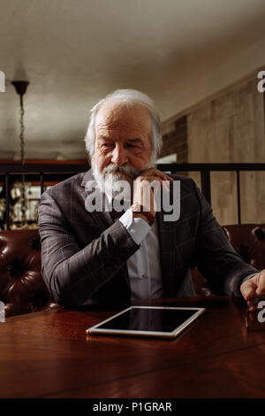 thoughtful rich old man sitting at the table Stock Photo