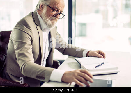 close up side view shot of senior chief sitting at work and using the tablet Stock Photo