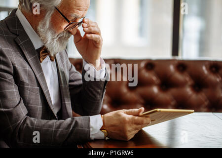grey haired man in glasses using iPad at home Stock Photo