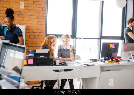 two young co-workers are gossiping. converse in murmurs. fan the breeze Stock Photo